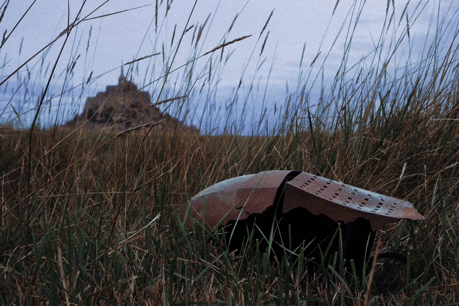 A broken knight's helmet abandoned in tall grass, a castle rock on the horizon