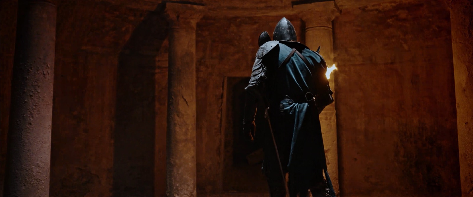 The Juggernaut knight walking through a torch-lit cloister